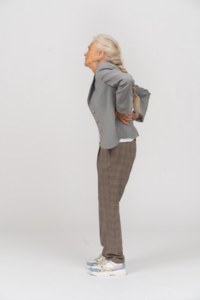 Вид сбоку на пожилую женщину в костюме, страдающую от боли в спине