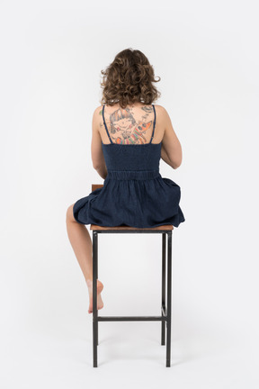 Garota com as costas tatuadas sentada de costas para a câmera