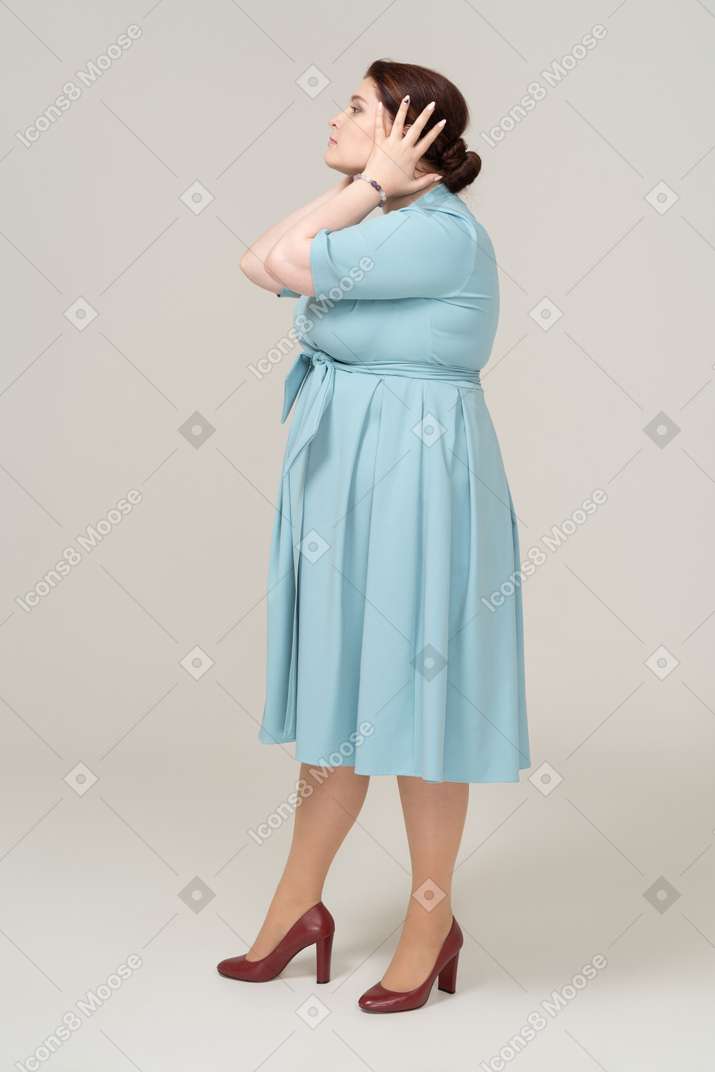 손으로 귀를 덮고 있는 파란 드레스를 입은 여성의 옆모습