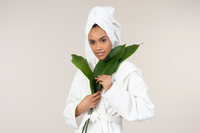 Mujer negra con bata blanca y toalla para la cabeza disfrutando de su rutina de cuidado de la piel