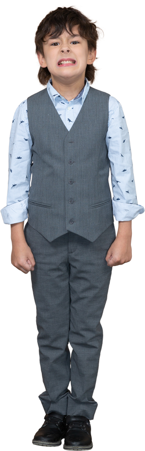 Vista frontal de un niño enojado en traje gris de pie con los puños cerrados