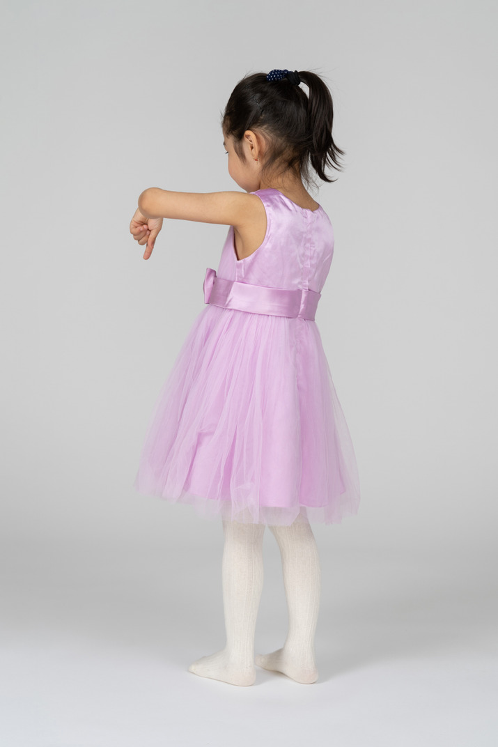 Three-quarter back view of a little girl pointing downwards