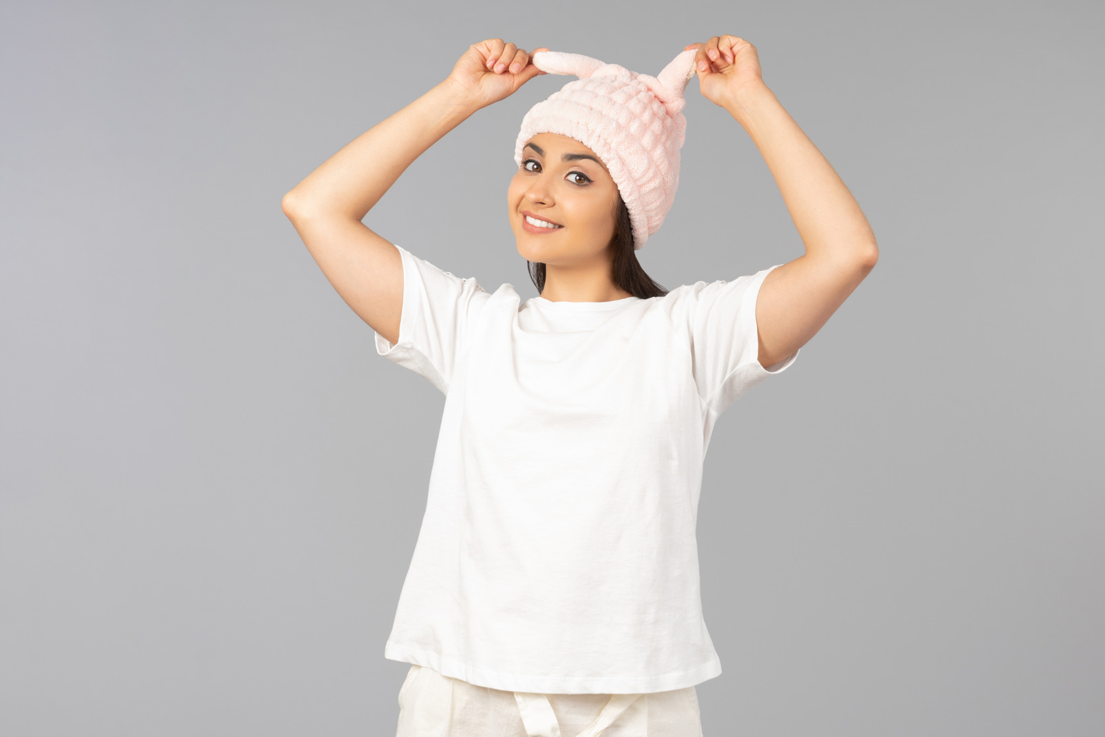 Young indian woman in home clothes touching pink rabbit like hat she's wearing