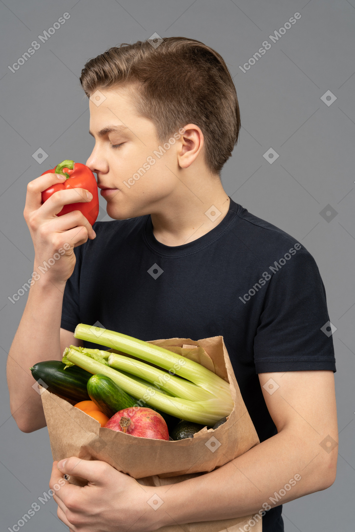 Young man smelling a red bell pepper