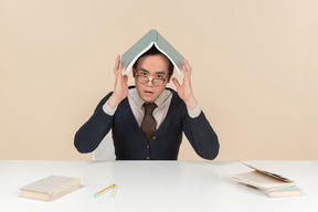 Young asian student in a sweater with a book on his head