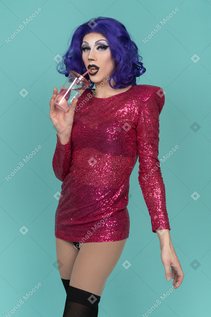 Ritratto di una drag queen in abito rosa con paillettes che beve un drink