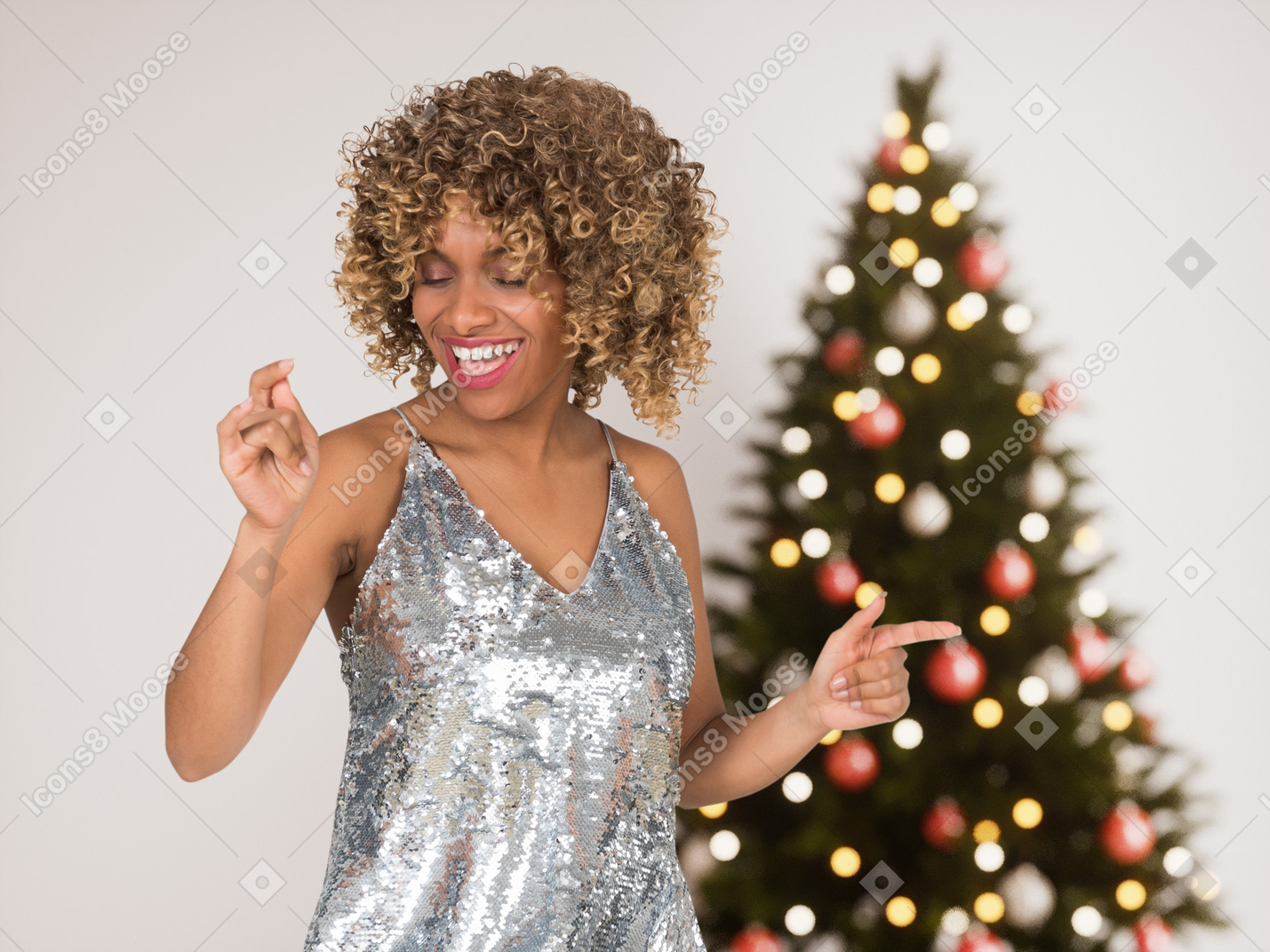 A woman in a silver dress standing in front of a christmas tree