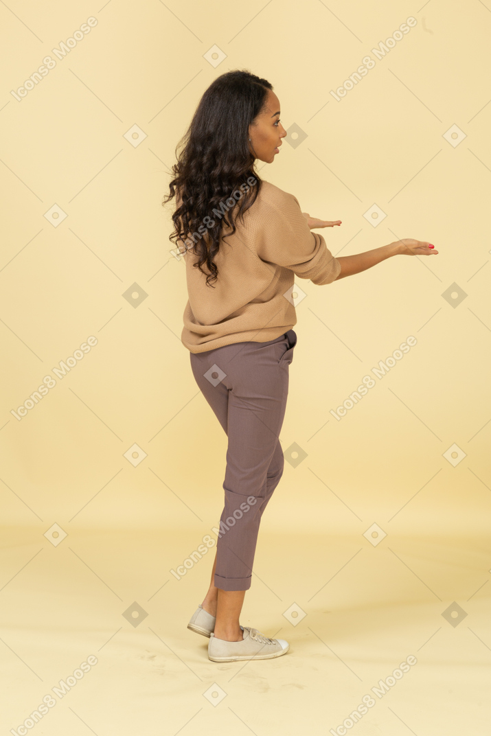 Vista posterior de tres cuartos de una mujer joven de piel oscura que cuestiona las manos extendidas