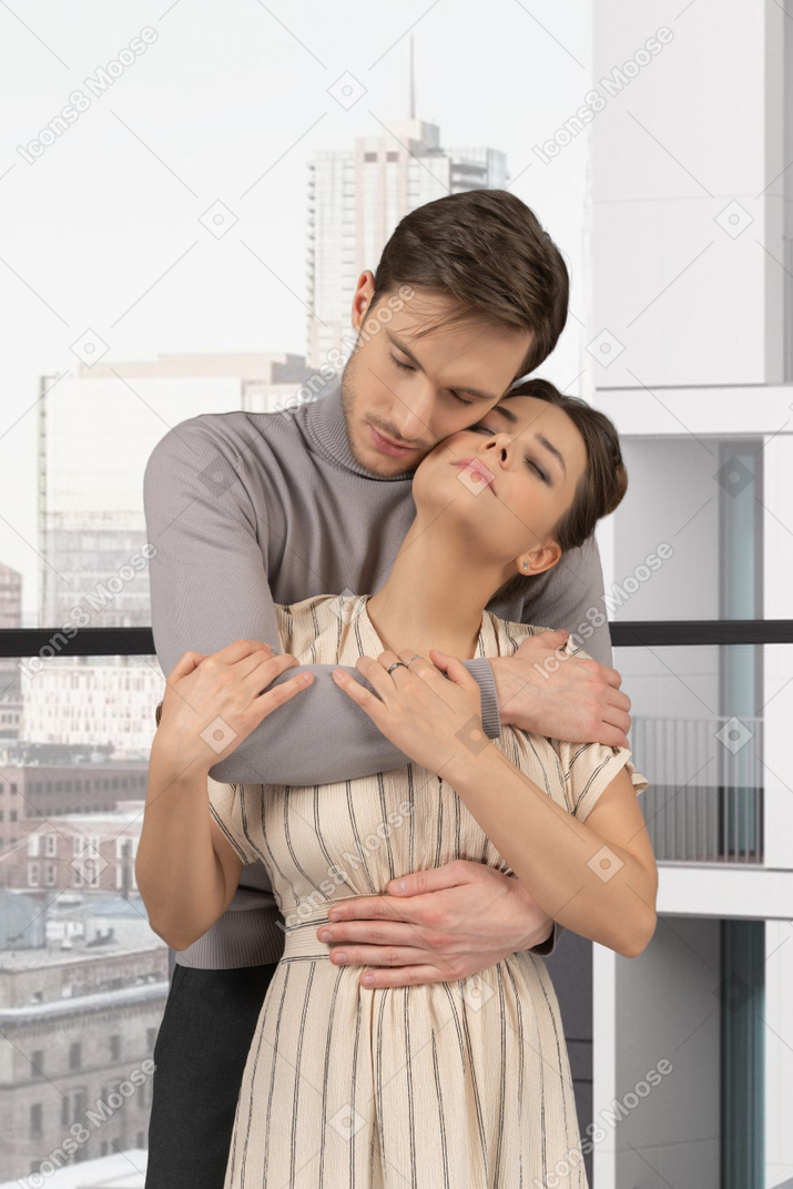 A man and woman embracing each other in front of a window