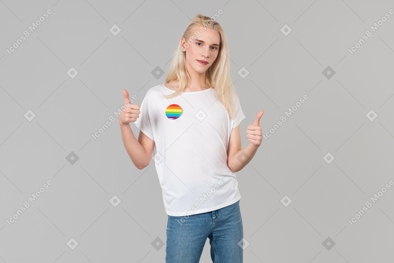 Good-looking young man with long blond hair, standing against grey background, wearing blue jeans and a white t-shirt with lgbt badge on it