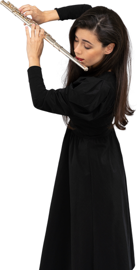 Vista di tre quarti di una giovane donna seria in abito nero che suona il flauto