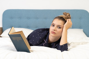 Vorderansicht einer jungen frau, die ein buch im bett liest