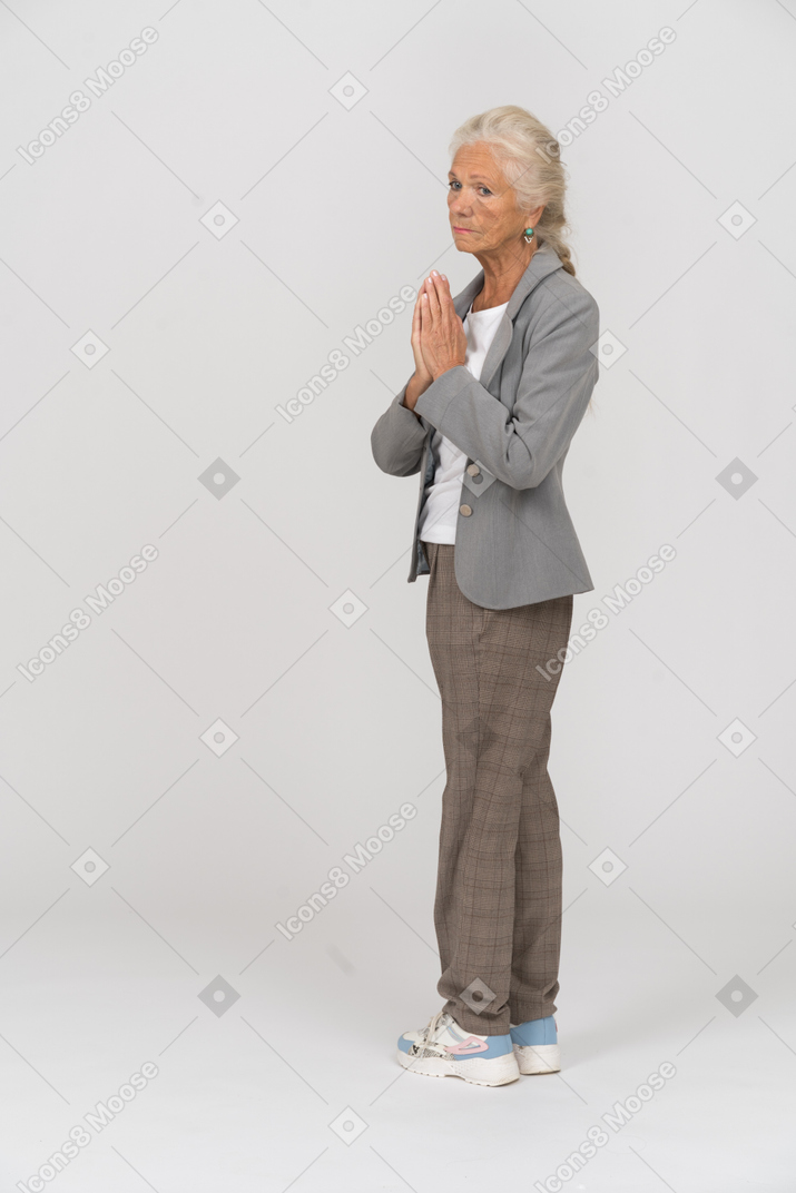 Vista lateral de uma senhora idosa de terno fazendo gestos de oração