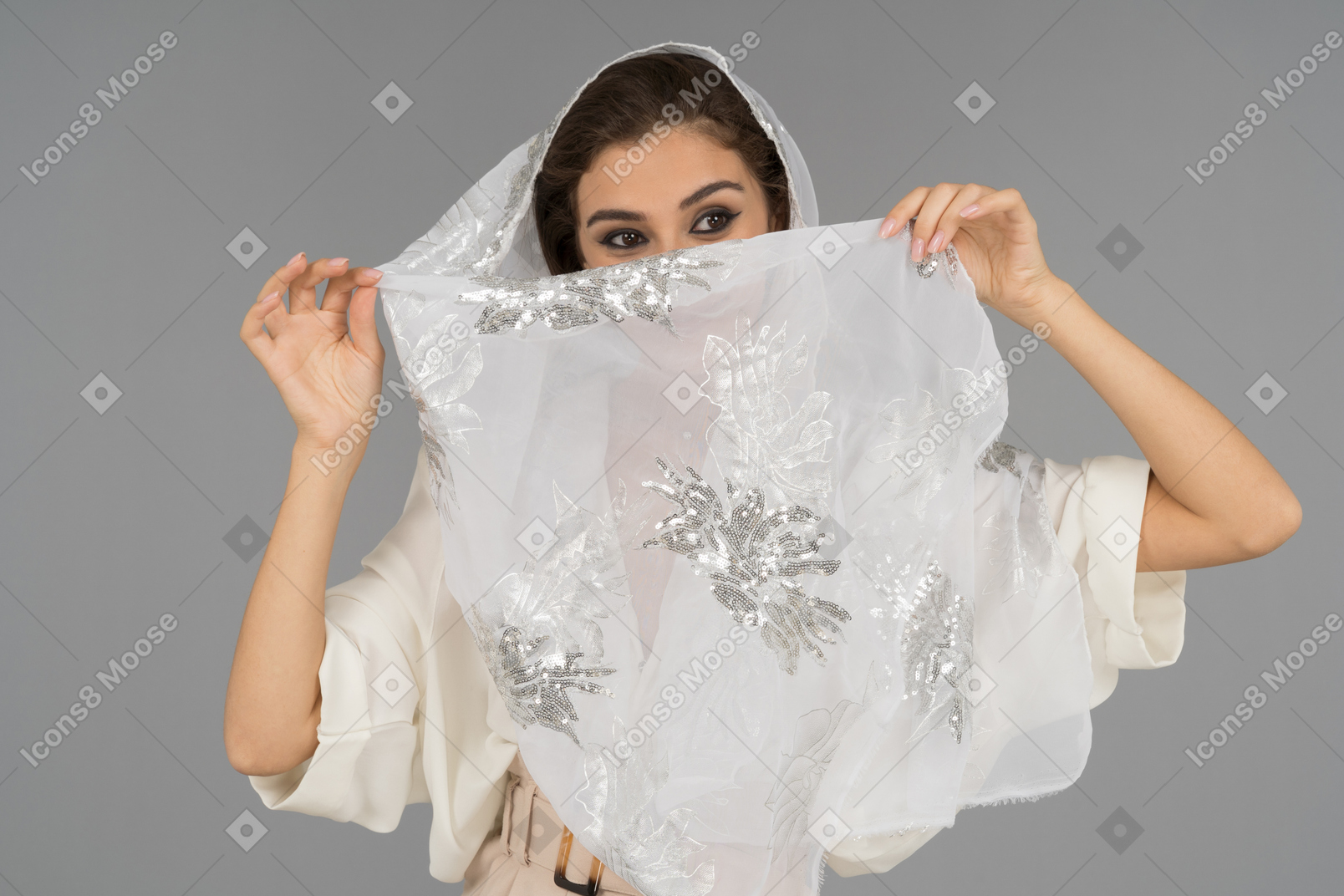 Cheerful young arab woman covering face with white shawl with silver embroidery