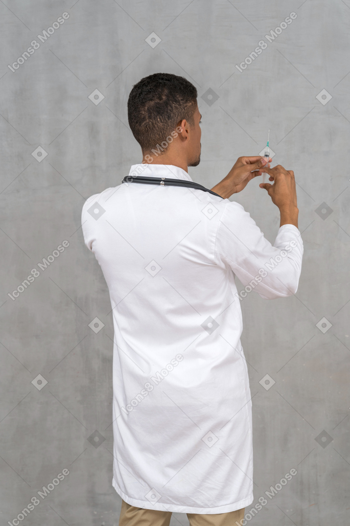 Back view of a male doctor holding a syringe