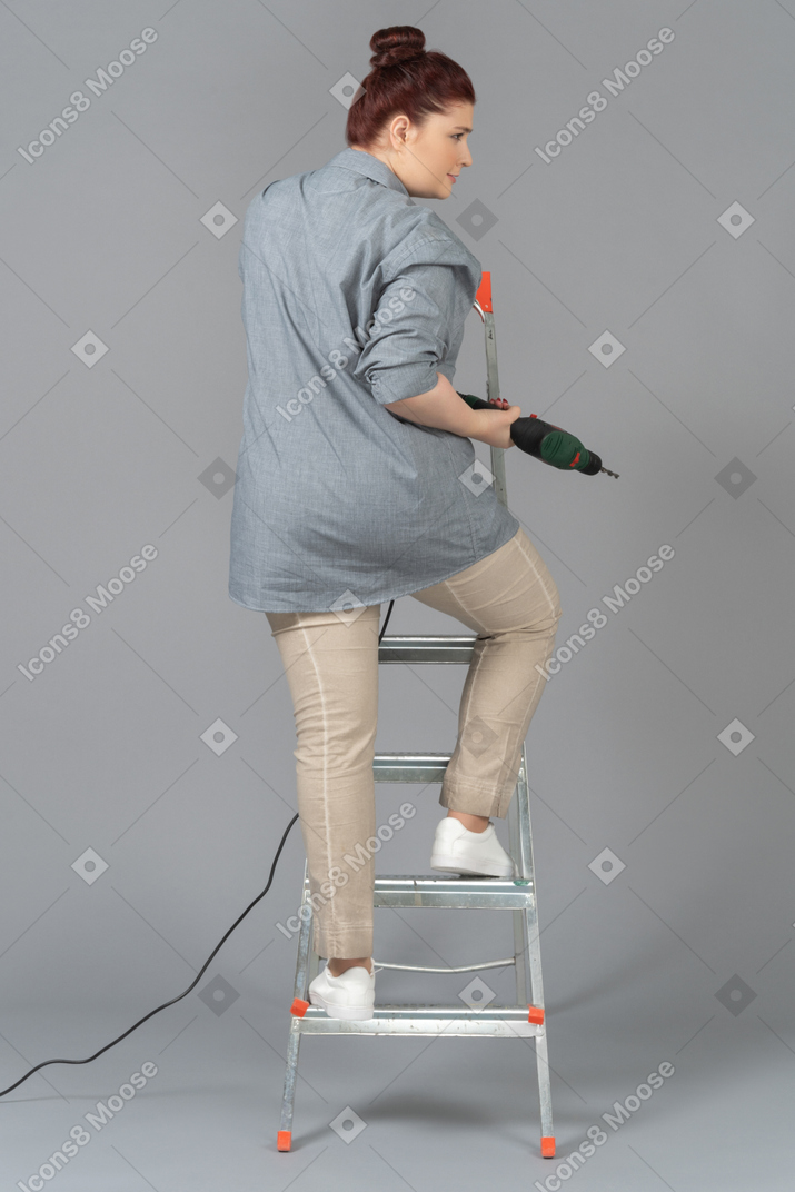 Woman standing on stepladder with a drill