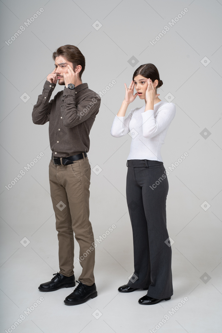 Dreiviertelansicht eines jungen paares in bürokleidung, die das gesicht berührt und die augen verengt