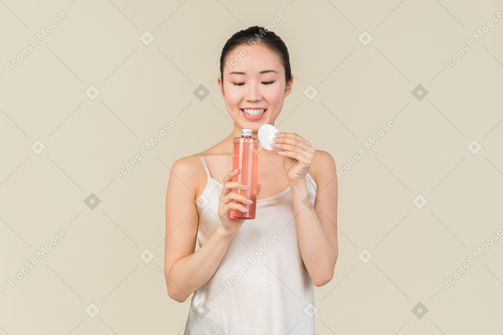 Dreamy young asian girl holding cosmetic bottle and cotton pad