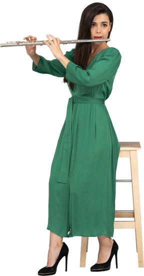 Comprimento total de uma jovem de vestido verde sentada em uma cadeira enquanto toca clarinete