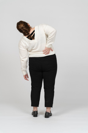 허리 통증으로 고통받는 흰색 스웨터에 통통한 여자의 후면보기