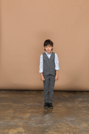 Vista frontal de un niño en traje parado y mirando a la cámara