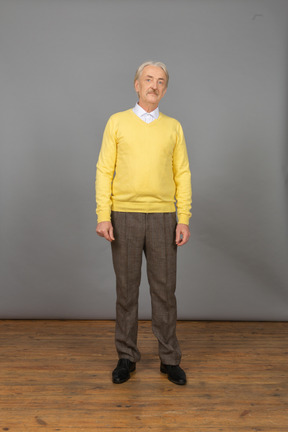 Vista frontal de um velho vestindo um pulôver amarelo e parado