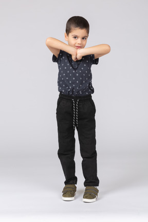 Vue de face d'un garçon mignon posant avec les mains devant la poitrine et regardant la caméra