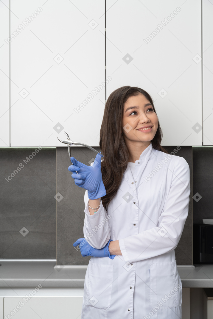 Front view of a female doctor holding her dental instrument and looking aside while smiling