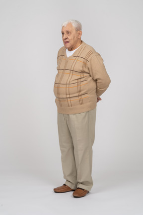 Front view of an old man in casual clothes standing with hands behind back