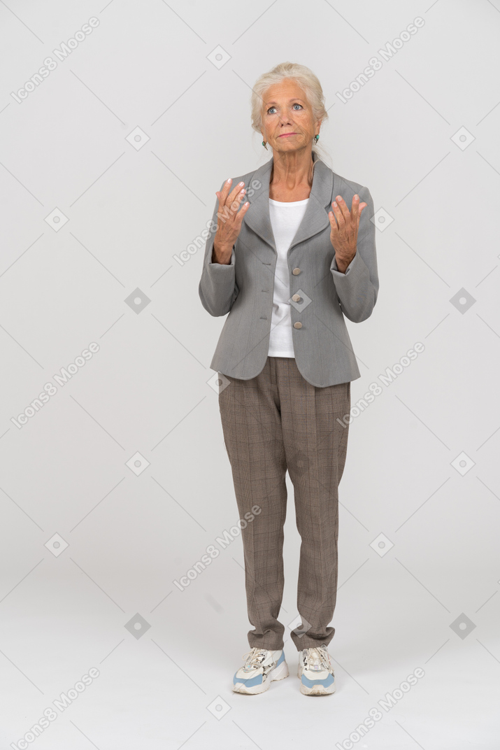 一位身着西装的老妇人举起双手站立的前视图