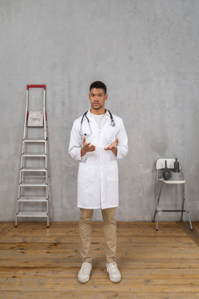 Front view of a young doctor standing in a room with ladder and chair explaining something