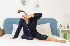 Vista frontal de una señorita en pijama poniéndose una máscara para dormir
