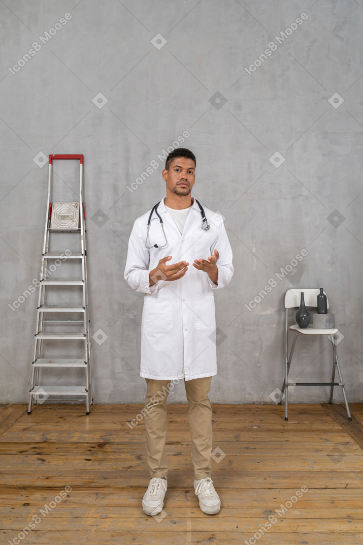 Vista frontal de um jovem médico em uma sala com escada e cadeira explicando algo