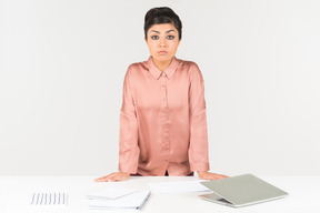 Young indian office employee standing at the table with laptop on it