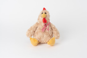 Un jouet de poulet en peluche avec un arc à damier, assis isolé sur un fond blanc