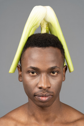 A shirtless young man with a celery on his head