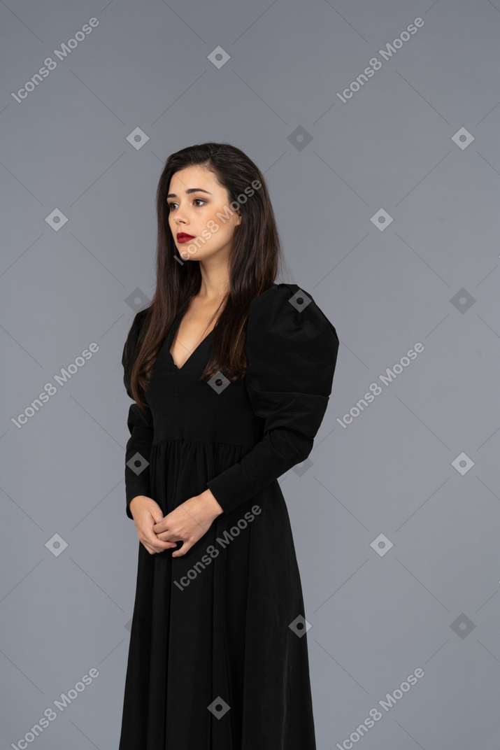 Vista di tre quarti di una giovane donna in un abito nero, tenendosi per mano
