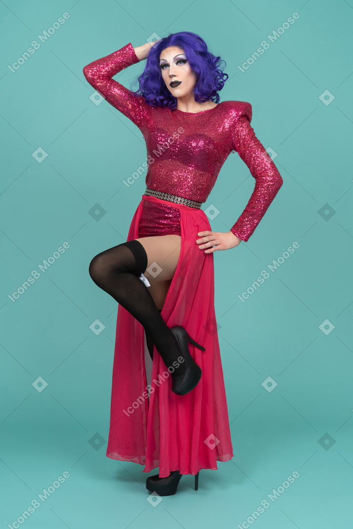 Drag queen in abito rosa in posa con la mano sull'anca e sollevando una gamba