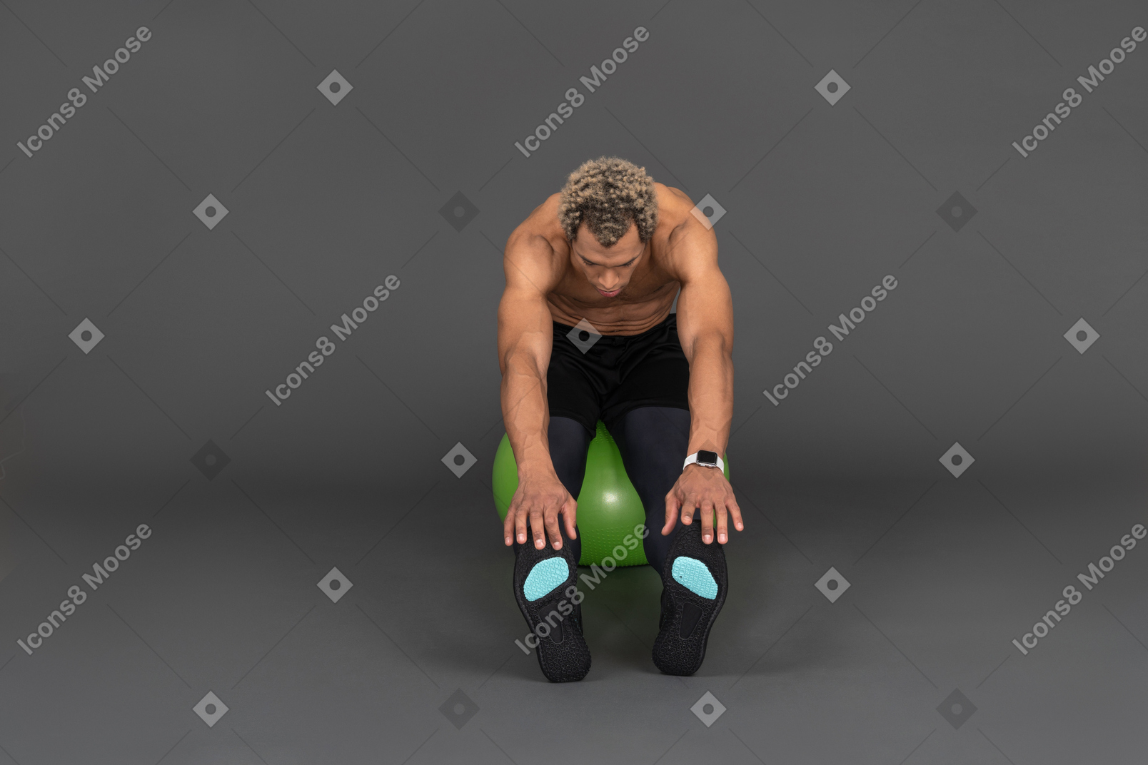 Vista frontal de un hombre afro sin camisa que se extiende mientras está sentado en una pelota de gimnasia verde