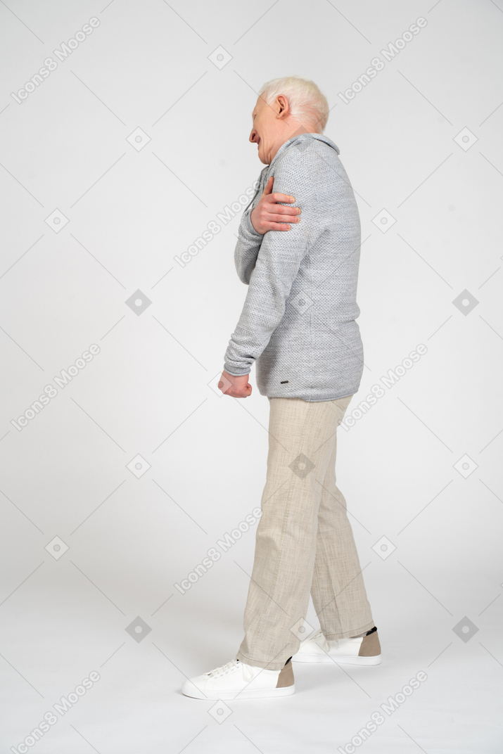 Вид сбоку на мужчину, стоящего и держащего плечо