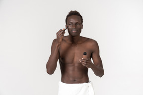 Um jovem negro com uma toalha de banho branca em volta da cintura fazendo sua rotina matinal