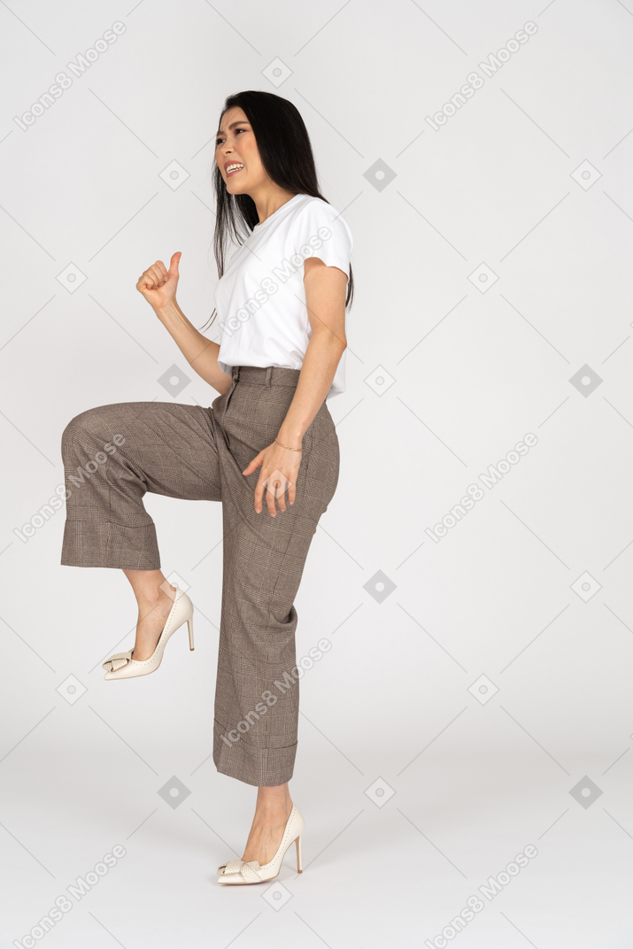 Vista di tre quarti di una giovane donna sorridente in calzoni e t-shirt alzando la gamba