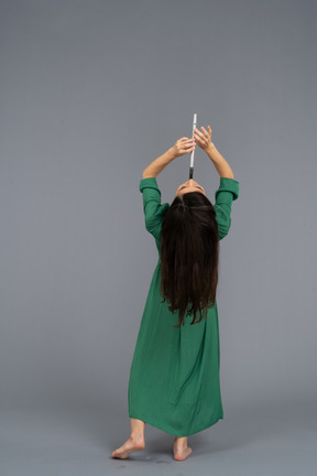 Back view of a young lady in green dress playing flute while leaning back