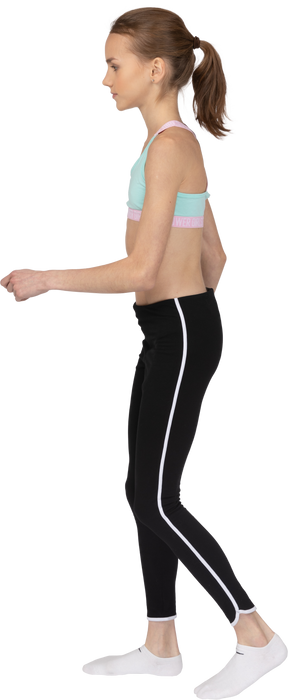 Vista lateral de una jovencita en ropa deportiva caminando y levantando la mano