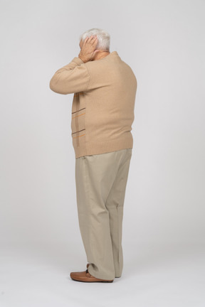 Side view of an old man in casual clothes covering ears with hands