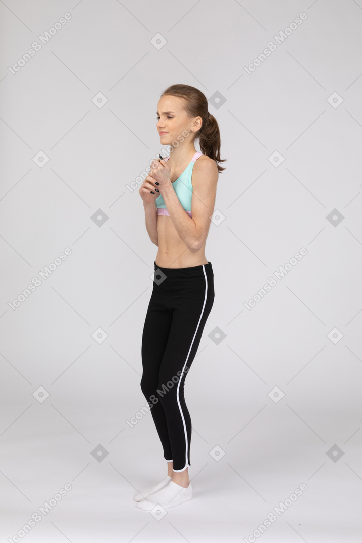 Three-quarter view of a displeased teen girl in sportswear holding hands together