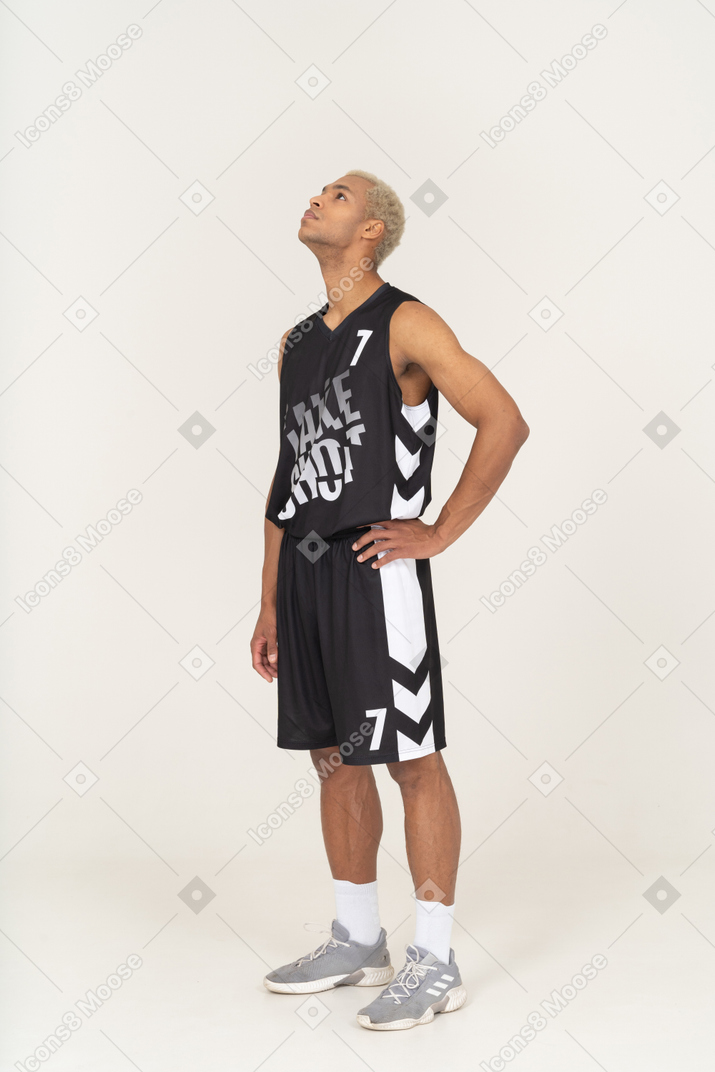 Dreiviertelansicht eines erwarteten jungen männlichen basketballspielers, der die hand auf die hüfte legt