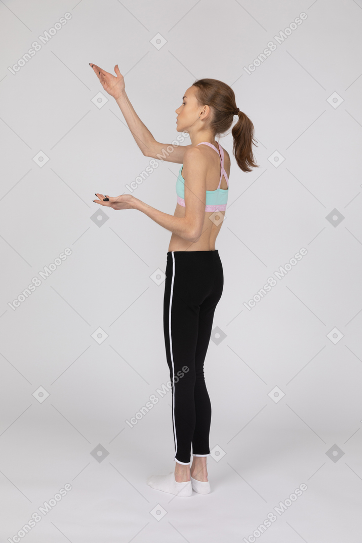 Three-quarter back view of a teen girl in sportswear raising hand and questioning