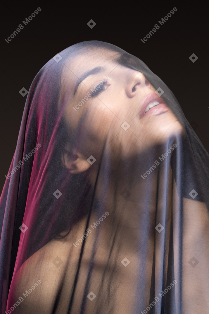 Close-up of sensual naked young woman in dark veil looking up