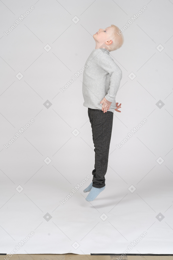 Vista lateral de un niño saltando mirando hacia arriba